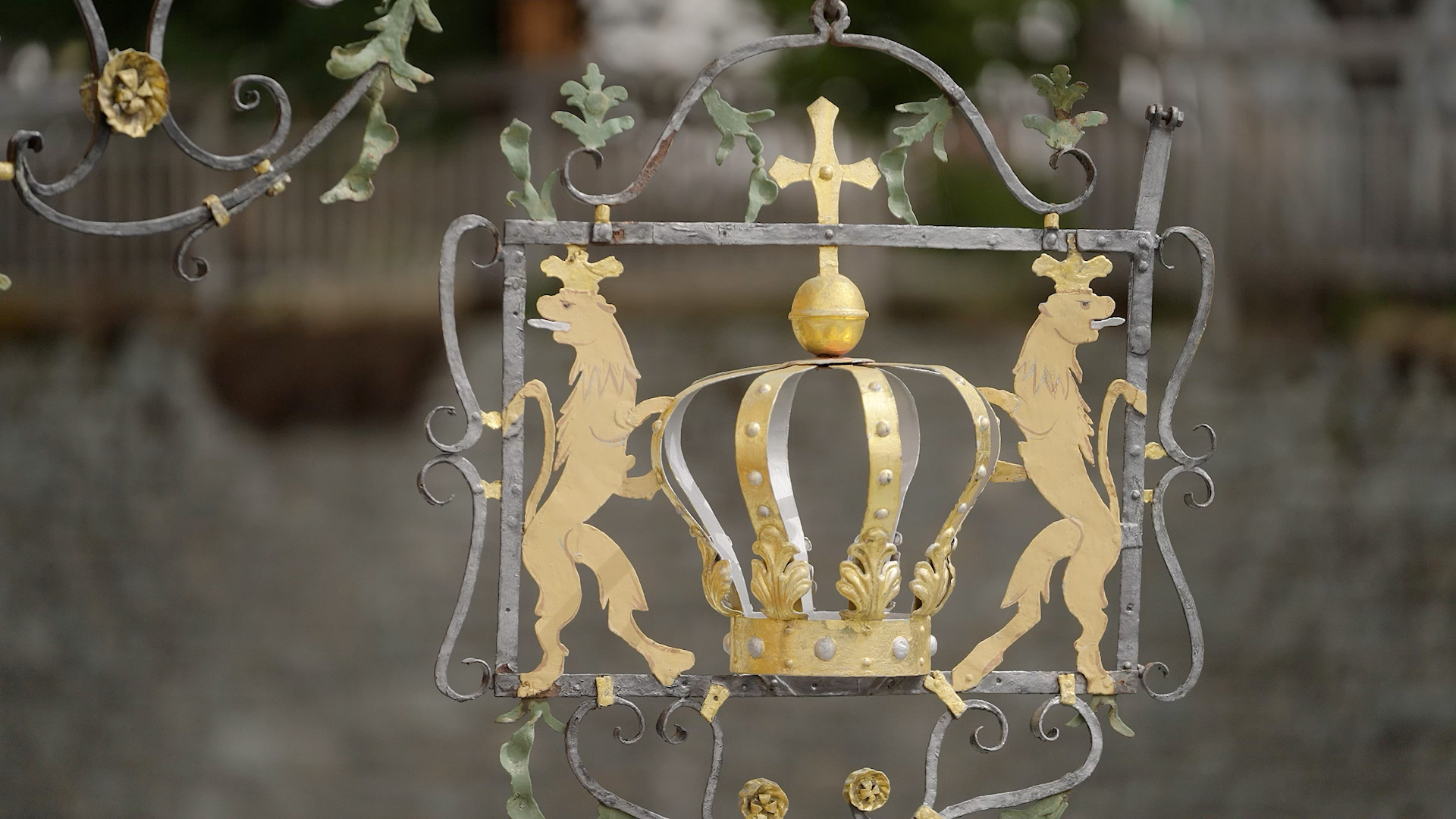 Königliches Wappenornament Geschmiedetes Schild mit goldener Krone und Löwenfiguren, umgeben von filigranen Details.